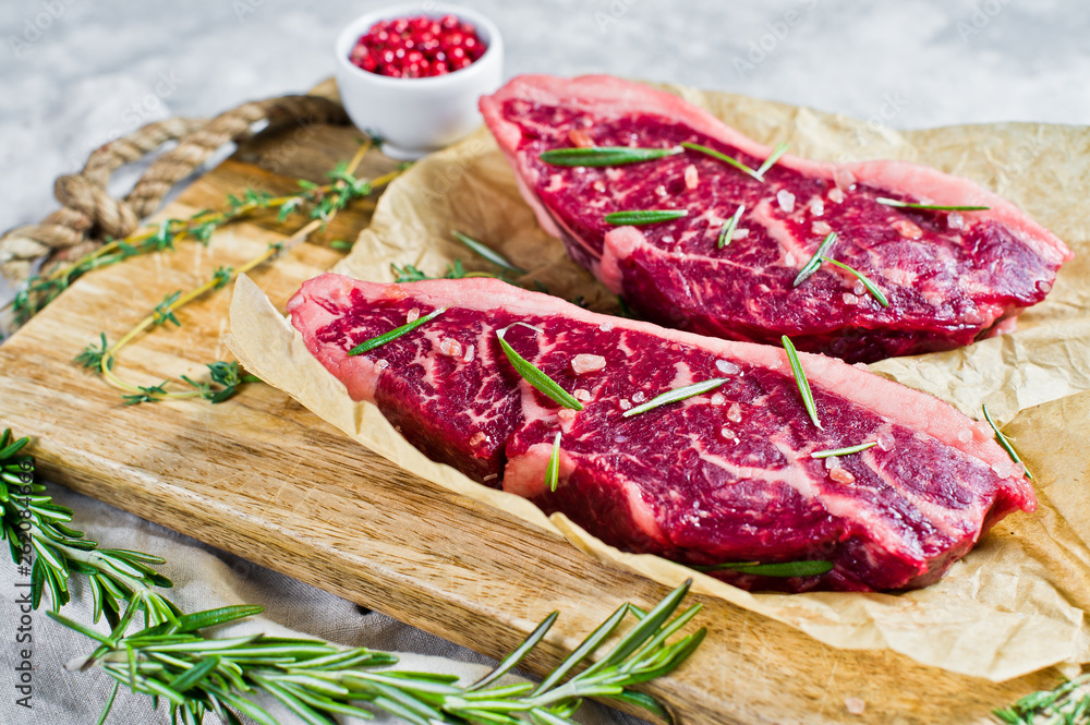 Beef sirloin steak on a wooden chopping Board with rosemary and pink pepper. Grey background, top view.