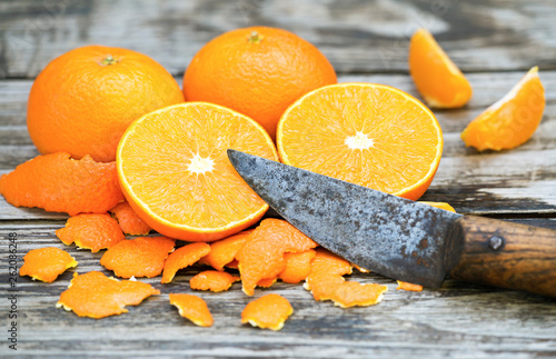 Whole and peeled fresh yellow mandarins with a sharp rustic knife on wooden background photo