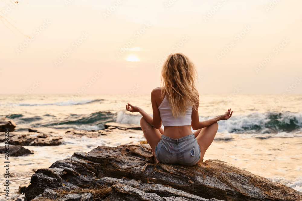 Young woman practicing yoga at the beach sea view at sunrise or sunset outdoors. Harmony and meditation concept. Healthy lifestyle