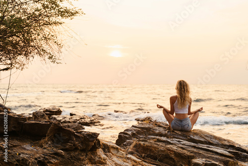 Young woman practicing yoga at the beach sea view at sunrise or sunset outdoors. Harmony and meditation concept. Healthy lifestyle