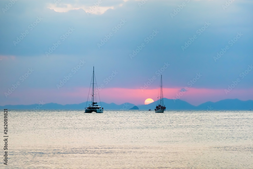 Three sailing yachts in the sea. During sunset, the sun sets over the mountains. Three sailing yachts in the sea. During sunset, the sun sets over the mountains.