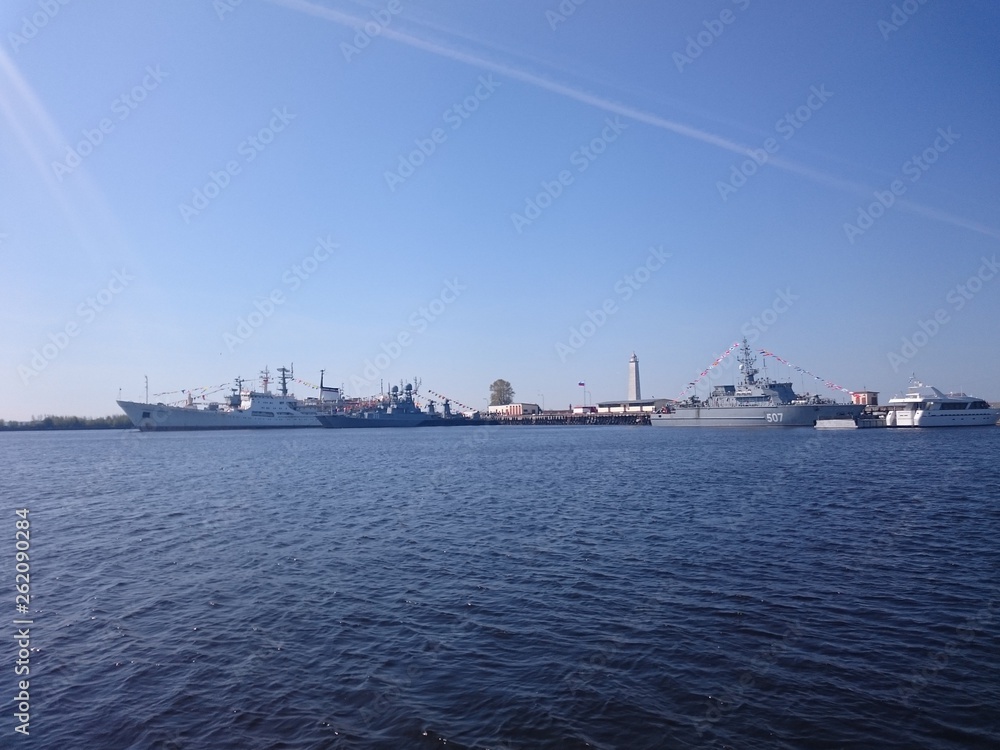 Ships on the water are in the port of Kronstadt, a clear day.