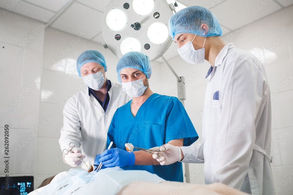 Group of surgeons at work operating in surgical theatre. Resuscitation medicine team wearing protective masks holding steel medical tools saving patient. Surgery and emergency concept. Group of surgeons at work operating in surgical theatre. Resuscitation medicine team wearing protective masks holding steel medical tools saving patient. Surgery and emergency concept.