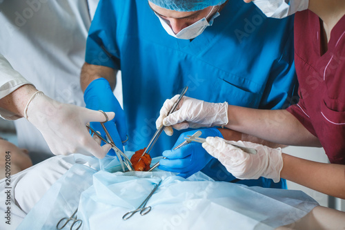 Group of surgeons at work operating in surgical theatre. Resuscitation medicine team wearing protective masks holding steel medical tools saving patient. Surgery and emergency concept.