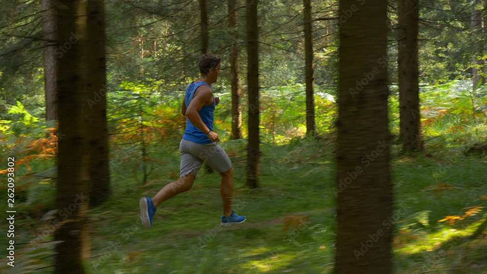Young Caucasian sportsman exercising by trail running through the cool woods