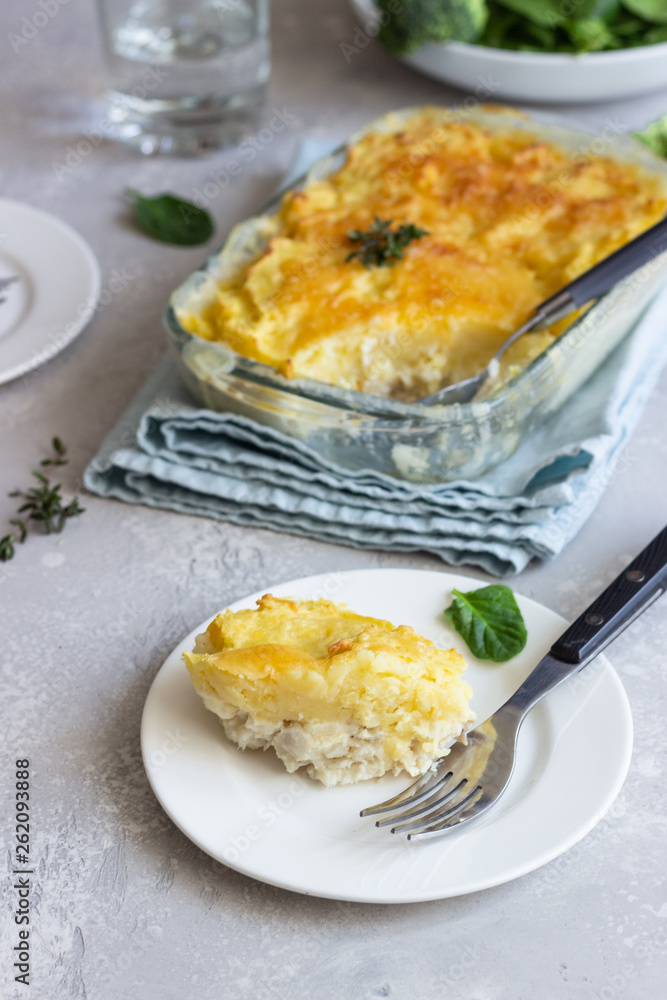 Potato casserole with fish and cheese on a light grey background.