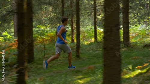 Young Caucasian sportsman exercising by trail running through the cool woods