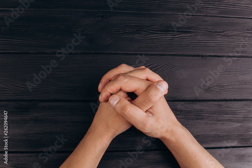 interlocked fingers, white male hands interlocked on black rustic wood table close up. top view. a man is waiting for negotiations