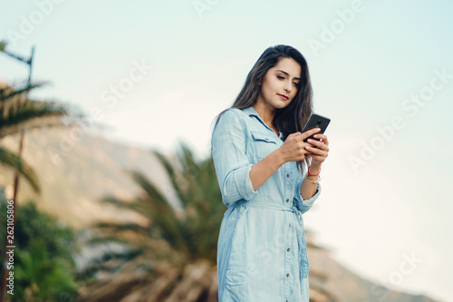 A beautiful young girl in a blue dress standing in a summer city and use the phone