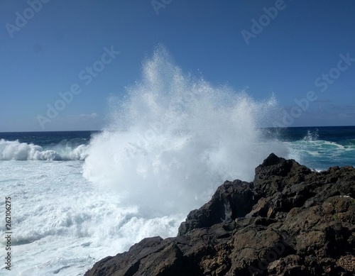 Welle bricht sich an einem Felsen im Wasser