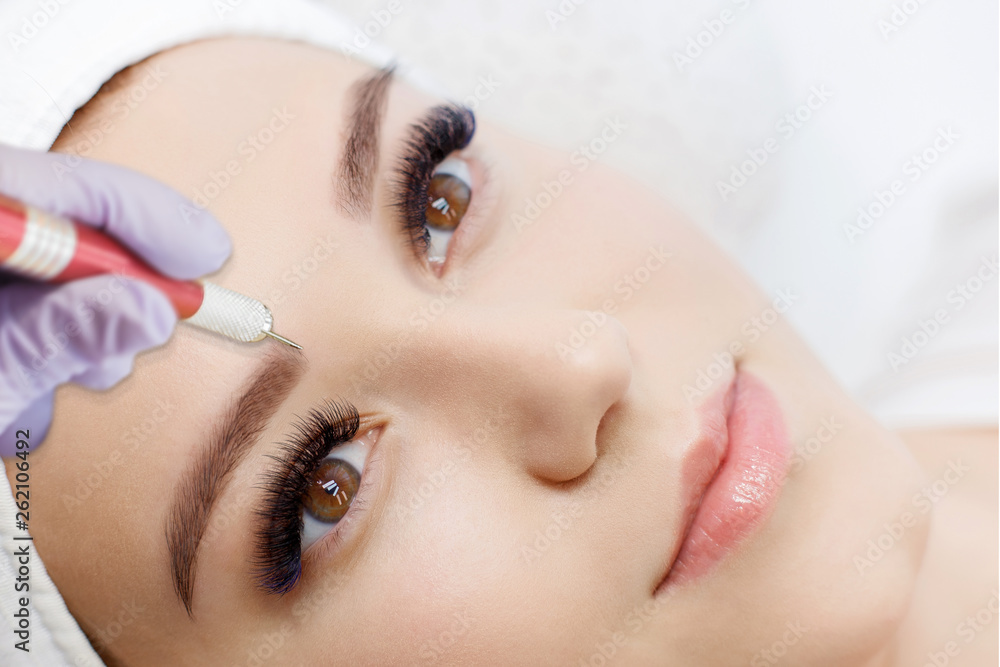 Beautiful young girl with long eyelashes tweezing her eyebrows in a beauty salon. Woman doing eyebrow permanent makeup correction . Microblading brow.