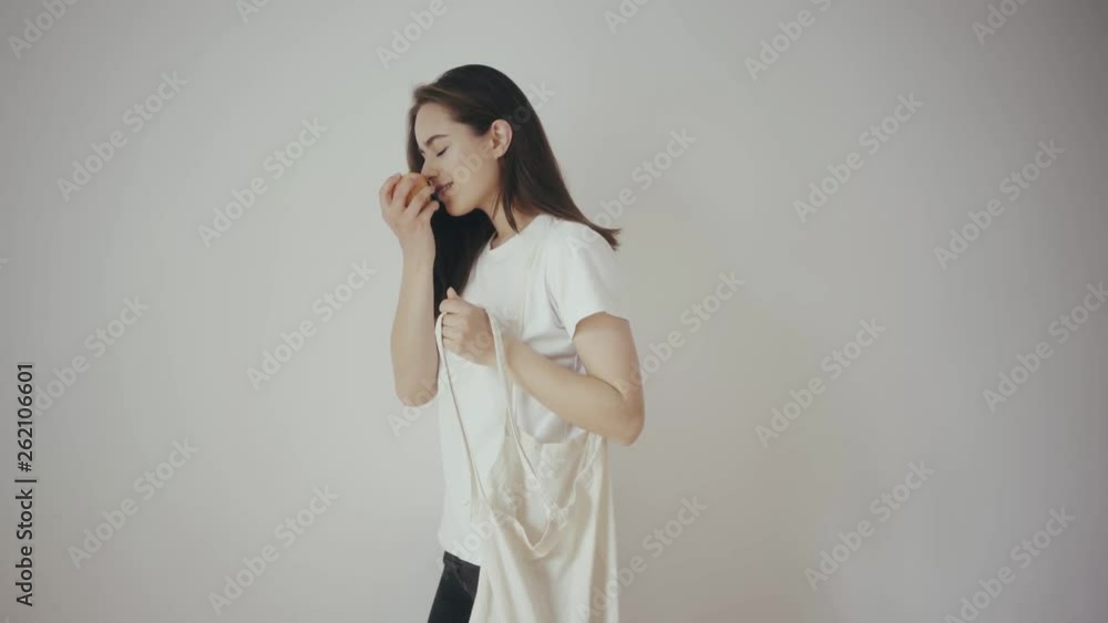 Young hipster smiling girl with white blank cotton shopper tote bag wearing white t-shirt and black jeans, mock-up of blank bag, white wall on the background, concept of shopping Young hipster smiling girl with white blank cotton shopper tote bag wearing white t-shirt and black jeans, mock-up of blank bag, white wall on the background, concept of shopping
