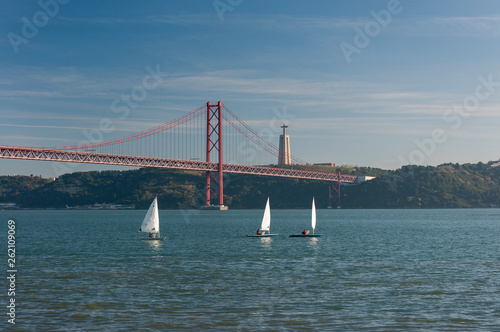 Three small sailing boats at the Tagus River with the 25 of April bridge on the background in the city of Lisbon, Portugal