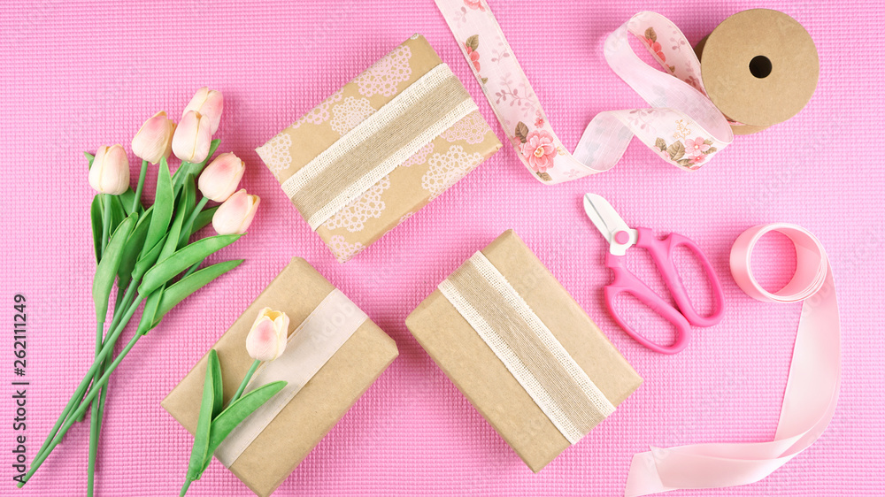 Gifts wrapped in kraft paper and pink ribbons overhead flat lay for Mother's Day, birthday or Valentine's Day celebrations. Gifts wrapped in kraft paper and pink ribbons overhead flat lay for Mother's Day, birthday or Valentine's Day celebrations.