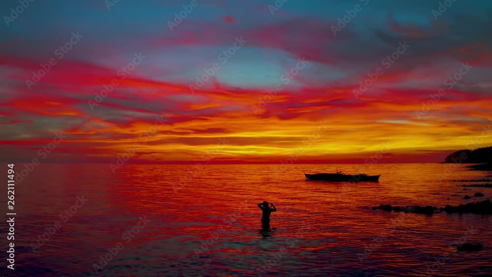 Free diving girl snorkeling in the sea reflecting crazy orange-yellow-pink sky looking like melted red hot metal on the background of the sea horizon and fisherman's boat silhouette, Philippines Free diving girl snorkeling in the sea reflecting crazy orange-yellow-pink sky looking like melted red hot metal on the background of the sea horizon and fisherman's boat silhouette, Philippines