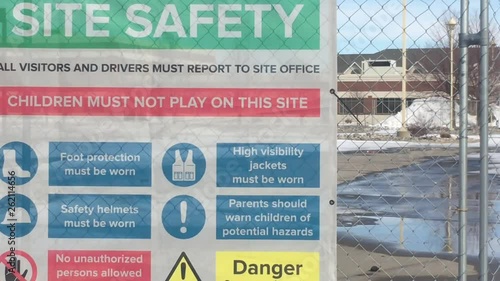 Site safety sign at construction site hanging on fence indicating dangers and being cautious. 