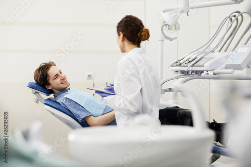 Portrait of smiling young man sitting in dentists chair during consultation, copy space