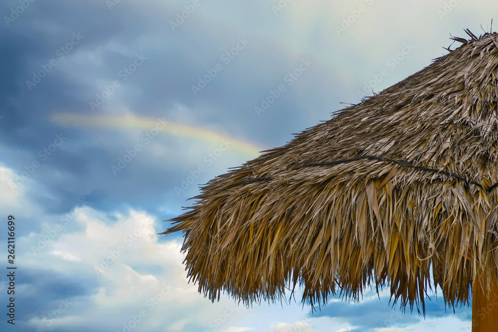 Fototapeta premium close up of tiki hut thatched roof with rainbow in sky background