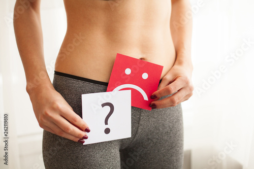 Vaginal or urinary infection and problems concept. Young woman holds paper with sad smile above crotch photo