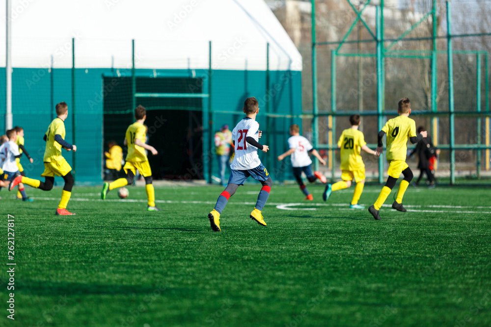 Obraz premium Boys in yellow white sportswear running on soccer field. Young footballers dribble and kick football ball in game. Training, active lifestyle, sport, children activity concept