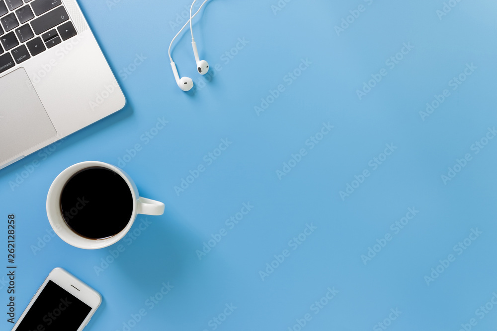 Listening to music at work. Flat lay desk top with laptop, earphone, coffee on blue background. Cool tone. - obrazy, fototapety, plakaty 