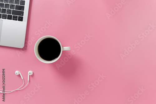 Listening to music at work. Flat lay desk top with laptop, earphone, coffee on pink background. Pastel tone..minimal desk style.