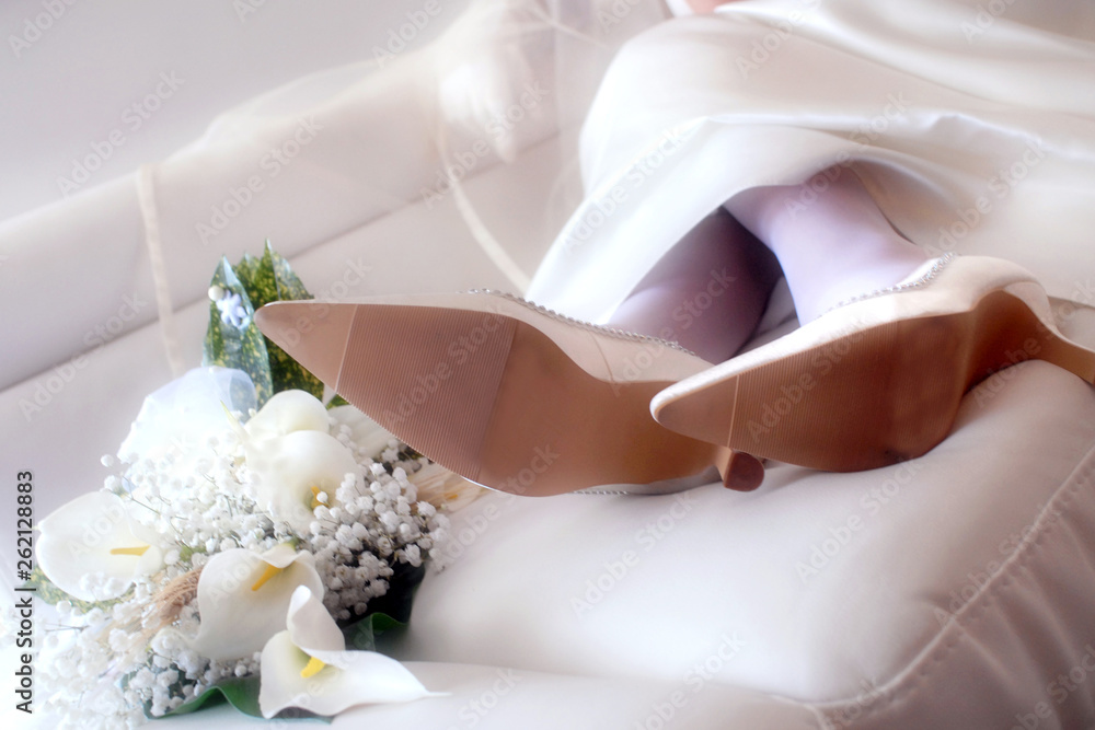Bride feet with shoes and bouquet relaxed on the white sofa Bride feet with shoes and bouquet relaxed on the white sofa