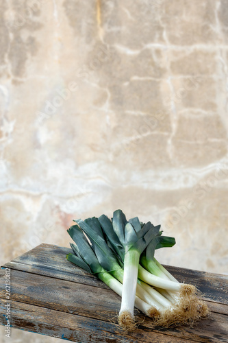 Fresh organic leeks tied on an old wooden board, against old white wall