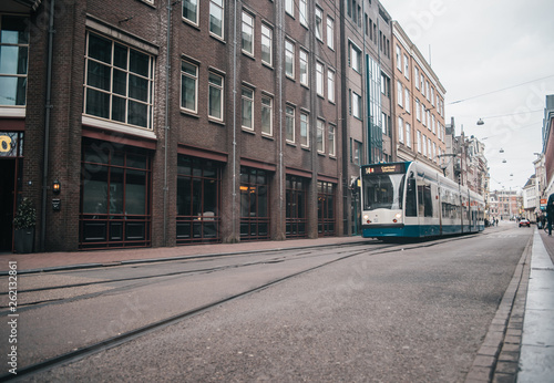 Modern public transport in Amsterdam, Netherlands. White and blue tram in old city.