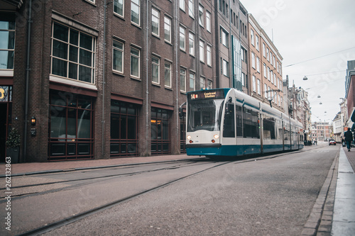 Modern public transport in Amsterdam, Netherlands. White and blue tram in old city.