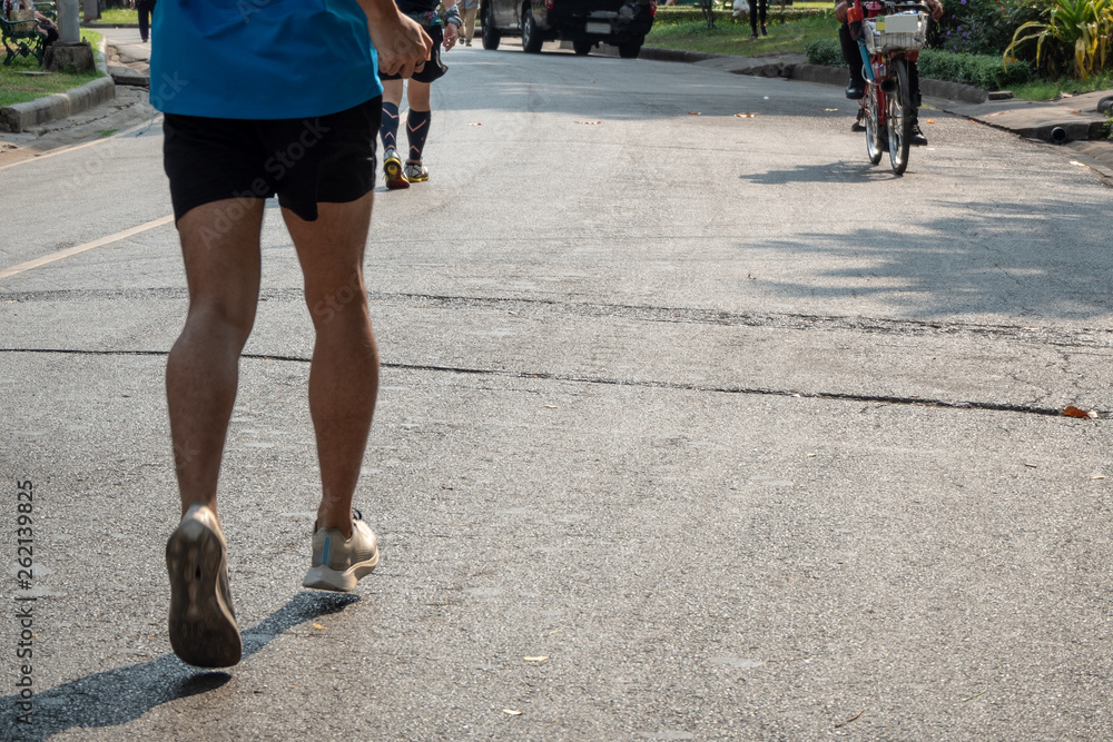 The bottom of the runner who wearing blue sport shirt and black sport shorts are jogging with many people are exercise in the city park  in the morning