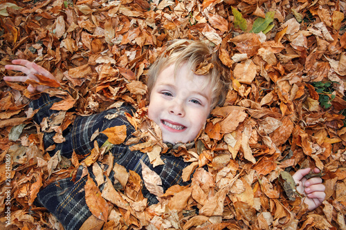 Cute young child laying buried in a pile of fall leaves