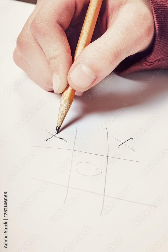 Closeup of a hand holding a pencil playing tic tac toe Closeup of a hand holding a pencil playing tic tac toe
