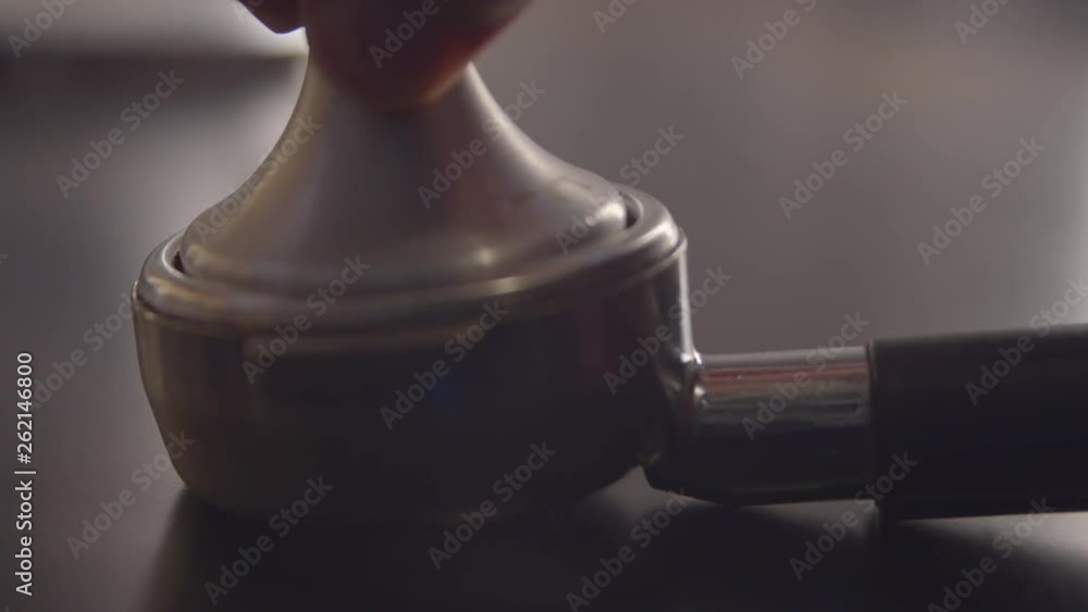 Slow motion Extreme close up shot of barista man hands pressing espresso coffee grounds into industrial machine brew basket with metallic press Slow motion Extreme close up shot of barista man hands pressing espresso coffee grounds into industrial machine brew basket with metallic press