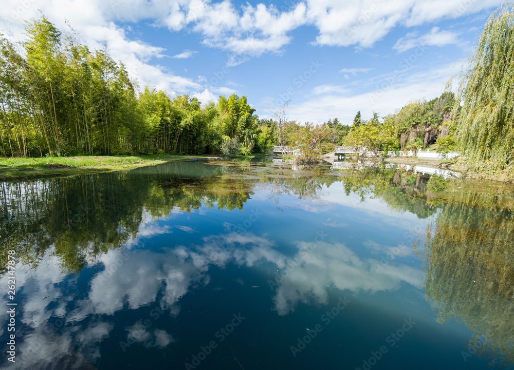 Fototapeta premium A pond with trees on the shores. Reflection of blue sky with clouds in water.