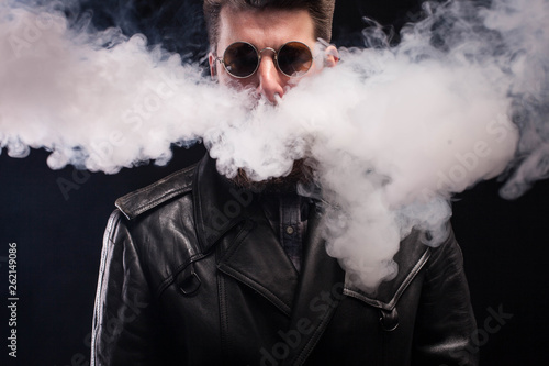 Cigarette smoking coming out of handsome bearded man nose over black background