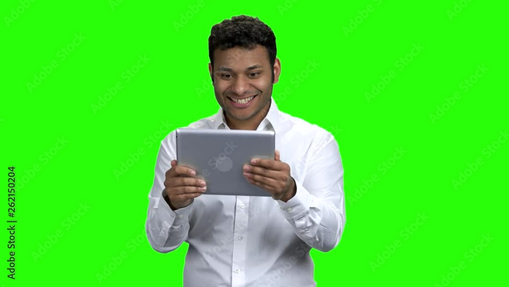 Surprised man looking at digital tablet. Young Indian man talking via computer tablet with surprise expression. Green screen background. Surprised man looking at digital tablet. Young Indian man talking via computer tablet with surprise expression. Green screen background.