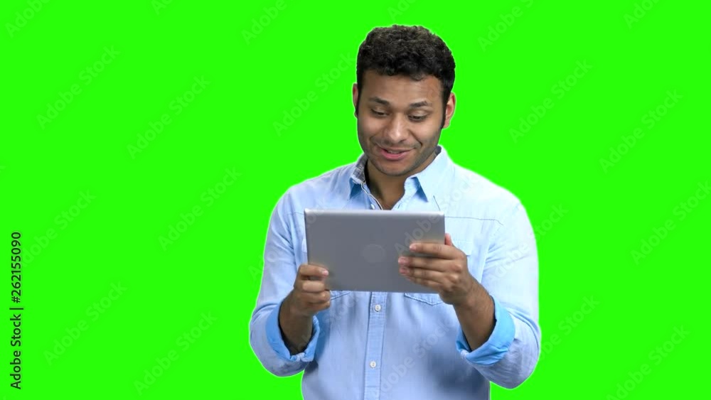 Cheerful Indian man with tablet pc on green screen. Happy excited young man talking via internet using digital tablet. Chroma Key background. Cheerful Indian man with tablet pc on green screen. Happy excited young man talking via internet using digital tablet. Chroma Key background.
