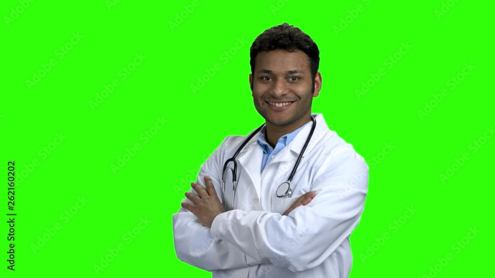 Portrait of smiling doctor puts on stethoscope. Friendly male doctor looking at camera with crossed arms. Chroma Key background.
