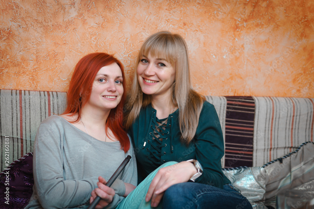 Two girls relax, have fun in the cafe. smoke hookah drink tea. The concept of smoking tobacco, refueling mix for hookah. Two girls relax, have fun in the cafe. smoke hookah drink tea. The concept of smoking tobacco, refueling mix for hookah.