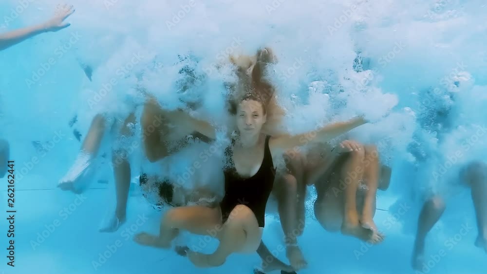 Underwater view of happy fun loving group of friends jumping and diving into swimming pool at a pool party in summer sunny day. Slow motion.