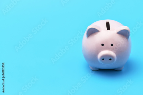 Pink piggy Bank in the shape of a pig is on the right blue background. On the left there is a place under the inscription. Piggy bank with copy space on blue background