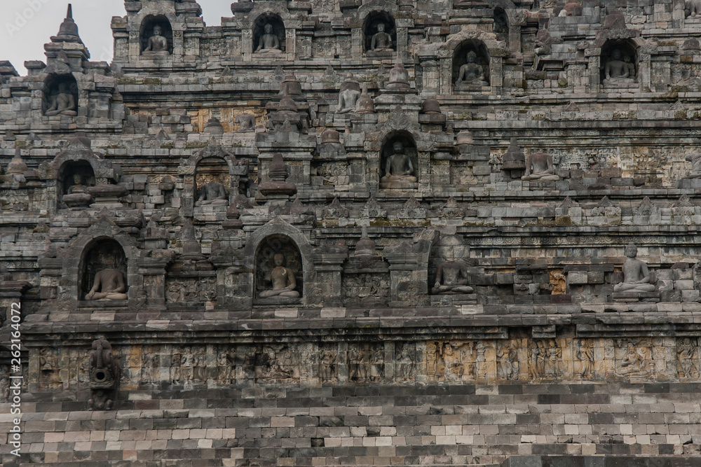 A fragment of the Borobudur Temple exterior with statues of seated Buddha in niches, Yogyakarta, Central Java, Indonesia