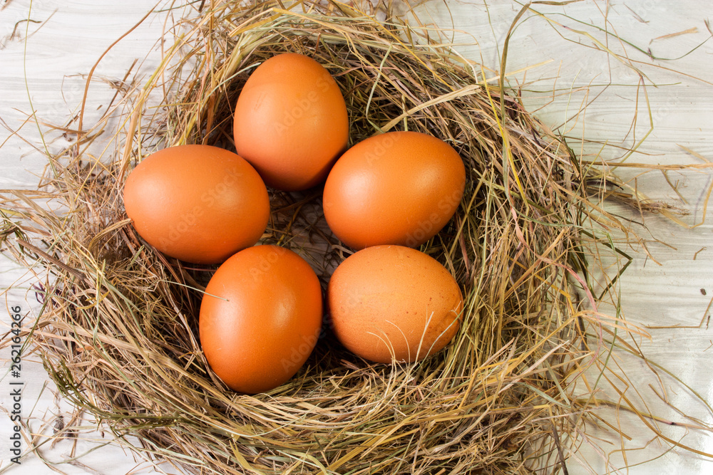 Five brown chicken eggs in a nest of straw on a wooden beige background. Five brown chicken eggs in a nest of straw on a wooden beige background.