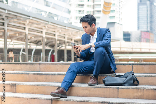 Smart young businessman watching cell phone in the city. Business, financial and technology concept.