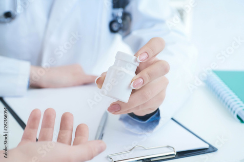 Female doctor hands gives jar of pills to patient hand closeup.