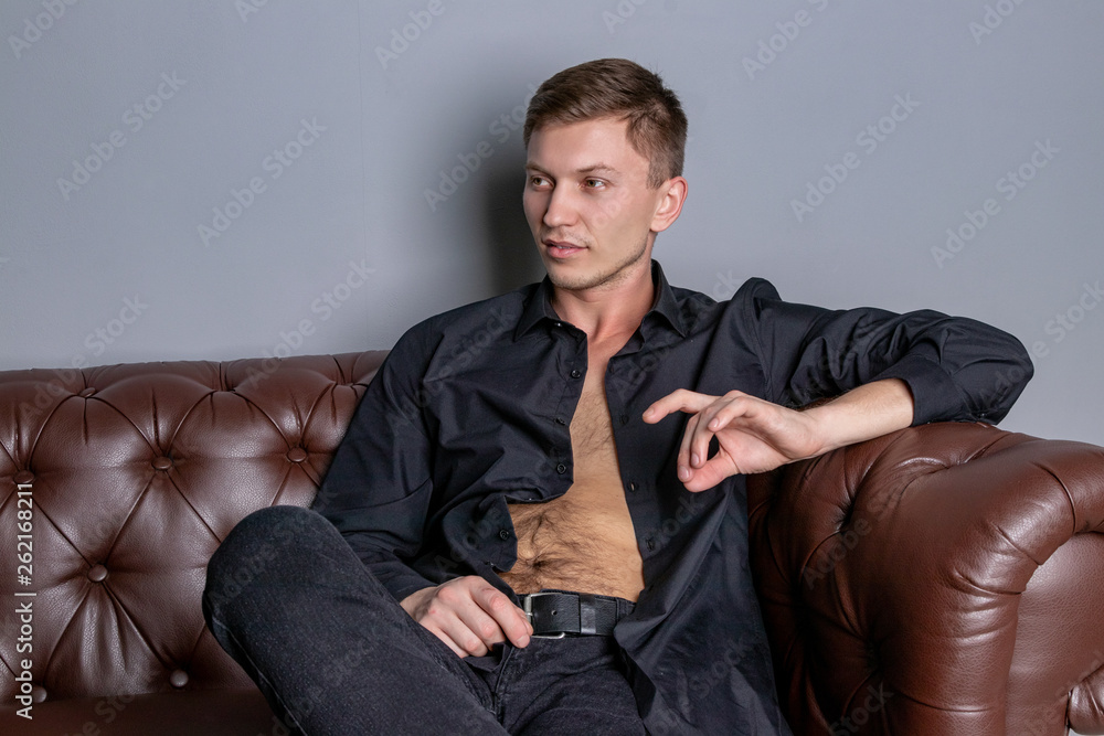 Sexy handsome man wearing black shirt sitting on the leather sofa. Comfort and relaxation