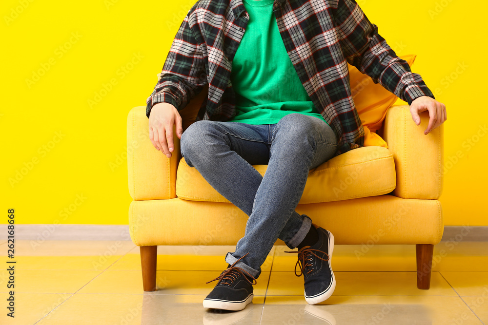 Stylish man in shoes sitting in armchair near color wall