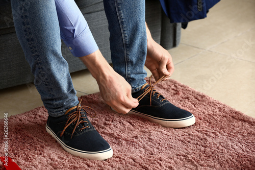 Young man putting on shoes in room