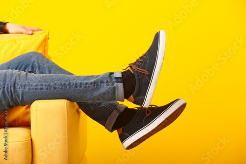 Stylish man in shoes sitting in armchair on color background